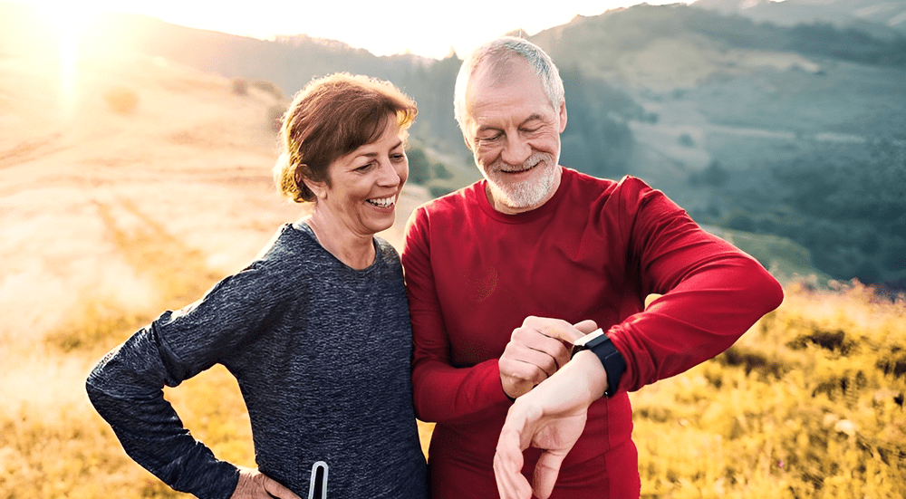 Older couple checking smartwatch outdoors, smiling.