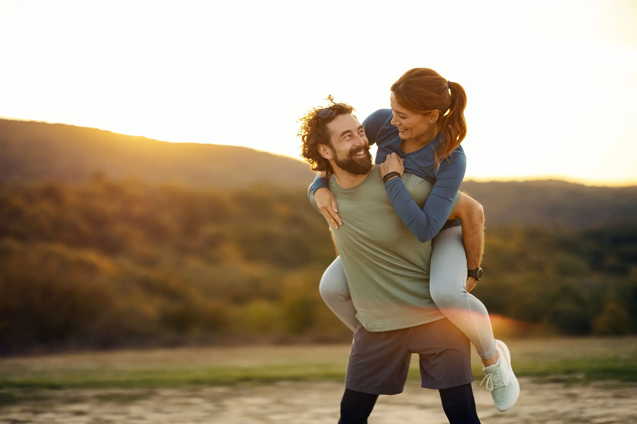Couple enjoying piggyback ride at sunset.