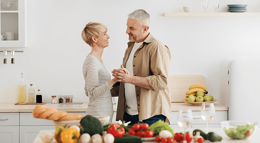 Couple dancing in kitchen with vegetables.