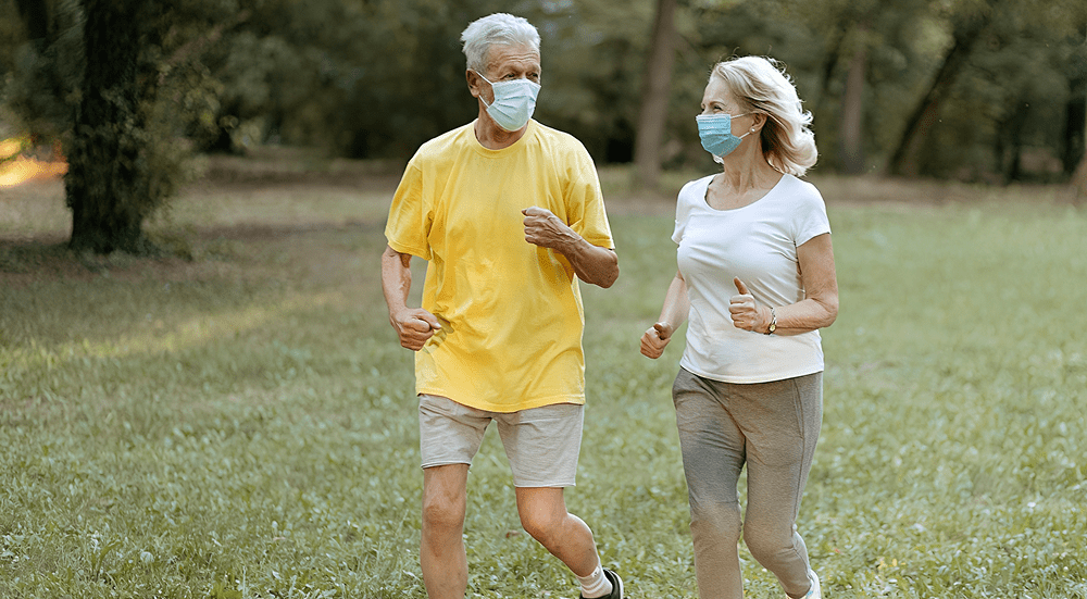 Elderly couple jogging with face masks outdoors.