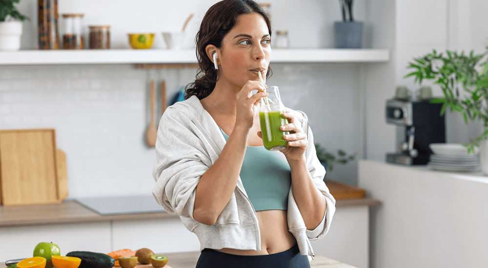 Woman drinking green smoothie in kitchen.