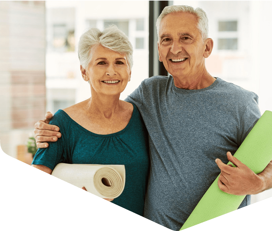 Senior couple holding yoga mats, smiling together.