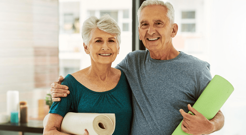 Smiling couple holding yoga mats indoors.