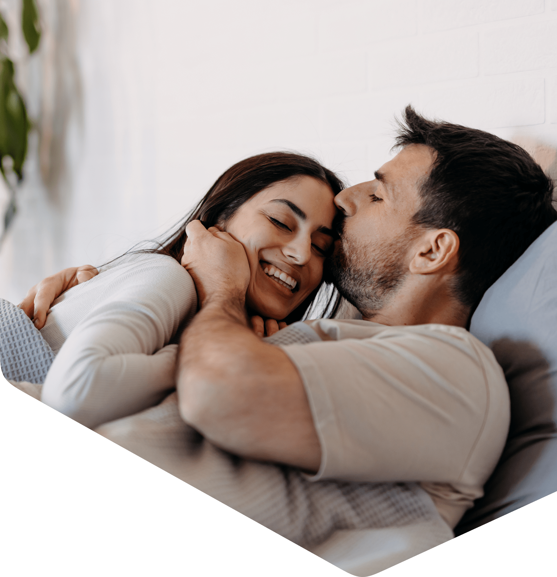 Couple cuddling in bed, smiling affectionately.